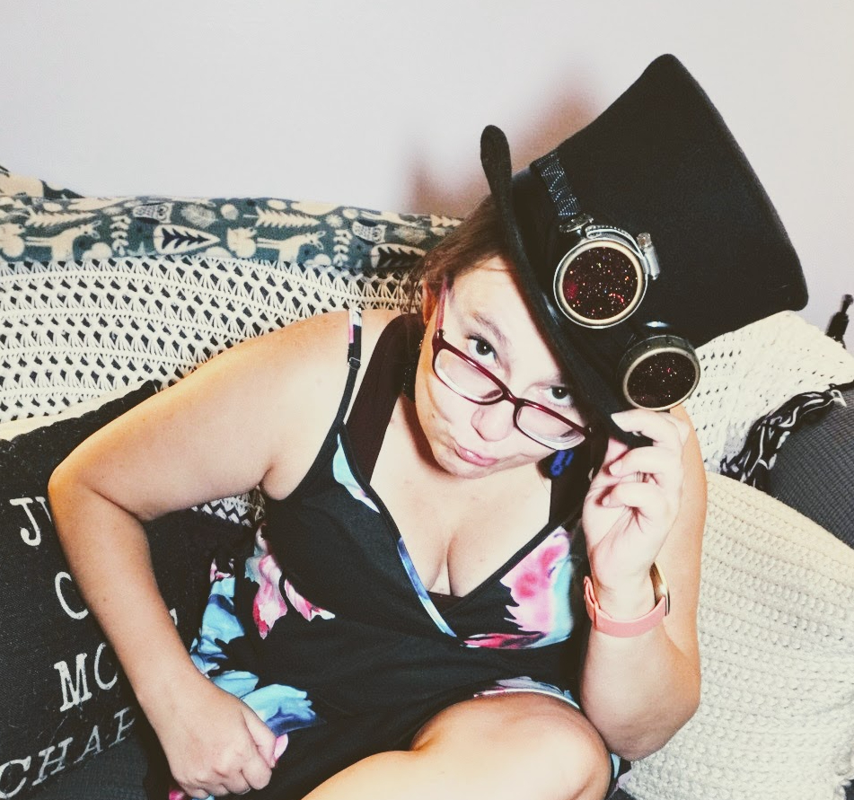 Liz, a white female presenting person, tips a top hat with goggles